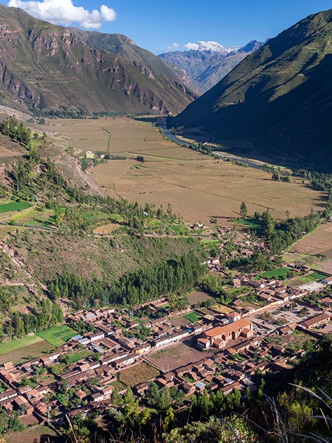 The town of Pisac and its fields on the valley floor, seen from high on a mountainside, snowy peaks beyond